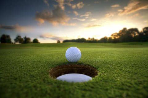 : Golf ball about to fall into the cup at sunset