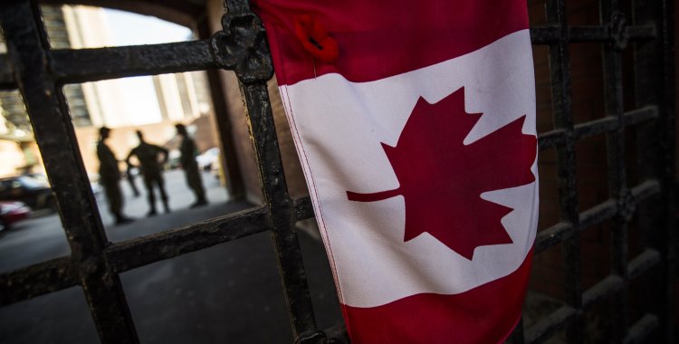 : Soldiers stand behind a Canadian flag at a makeshift memorial in honour of Cpl. Nathan Cirillo outside of The Lieutenant-Colonel John Weir Foote Armoury in Hamilton, October 23, 2014. A gunman attacked Canada's parliament on Wednesday, with gunfire erupti